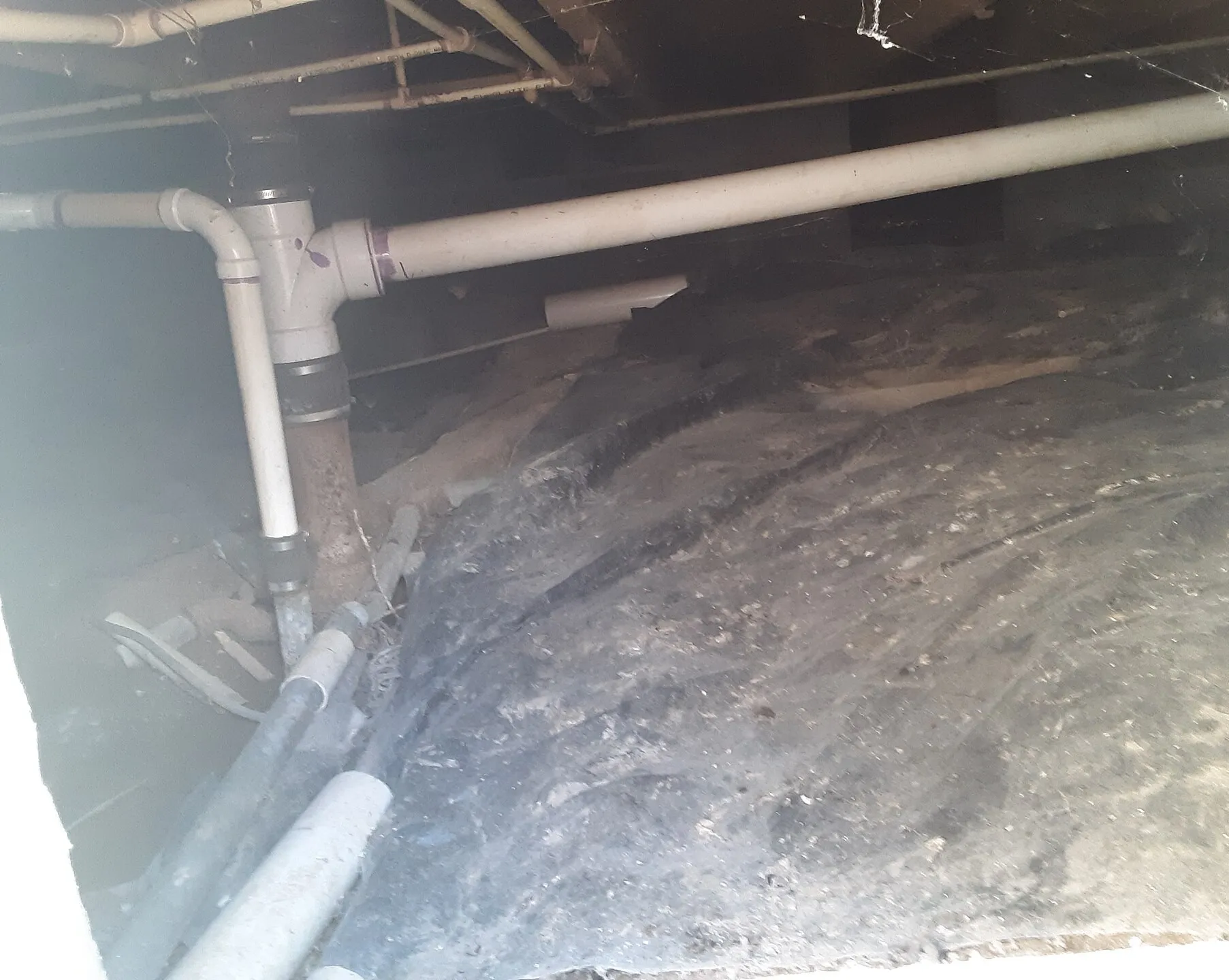 A crawl space seen through its access panel, with a plastic sheet laid partway over the dirt
